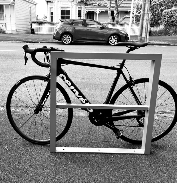 Square steel frame bike rack holding a road bike beside a street