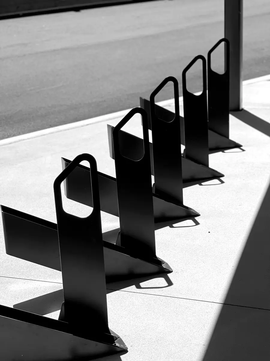 Row of five black steel bike racks on a sunlit footpath